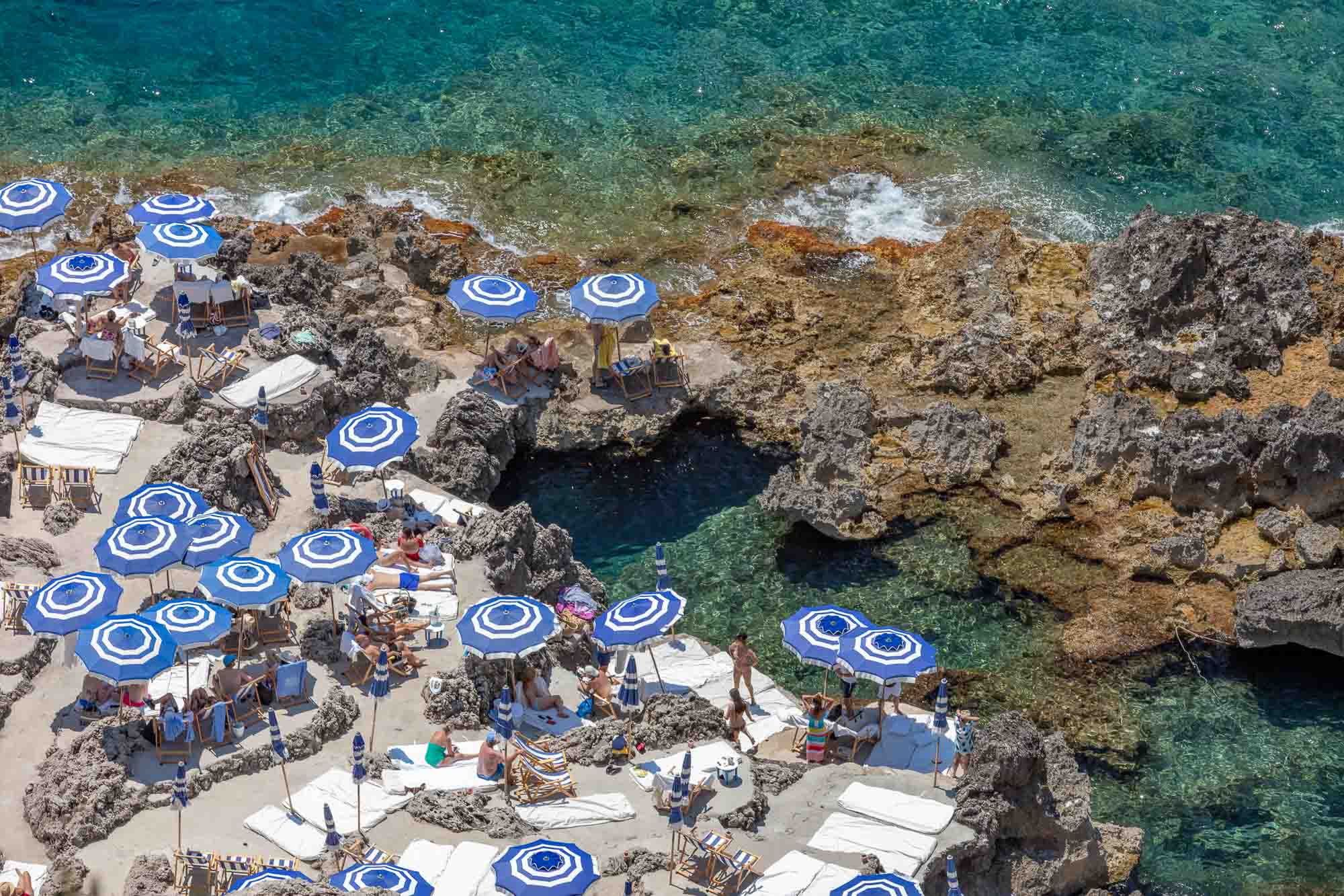 Beach scene with blue and white umbrellas on a rocky shoreline.